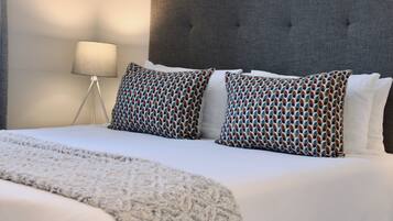 Een hotelkamer met een groot bed, een grijs gestoffeerd hoofdeinde en gekleurde kussens.