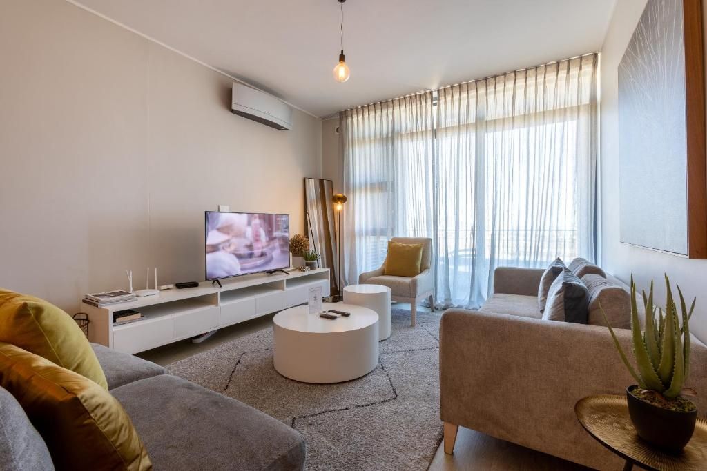 A modern living room with a flat-screen TV, a sofa, a coffee table, and a potted plant.