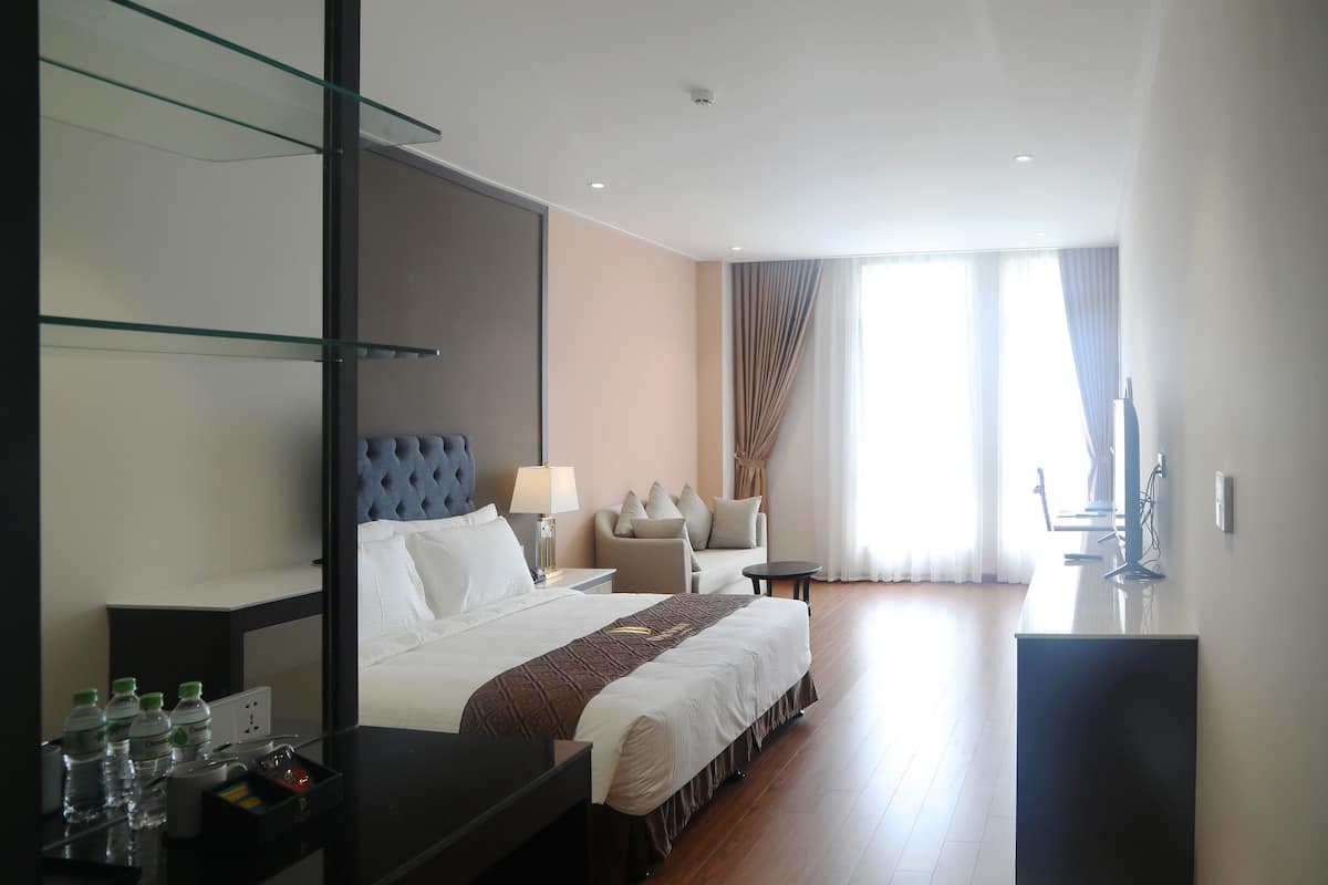 Ein Hotelzimmer mit einem großen Bett, einem Schreibtisch, einem Stuhl, einem Fernseher und einem Fenster mit Vorhängen.