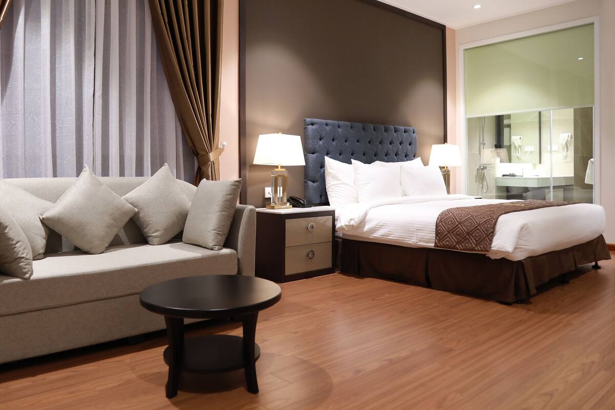 Ein Hotelzimmer mit Bett, Sofa, Nachttisch, Lampe und rundem Tisch.