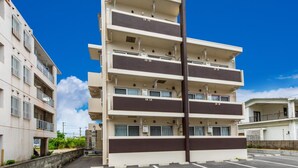 Un immeuble résidentiel à plusieurs étages, doté de balcons, d’un parking et surplombant un ciel bleu dégagé.