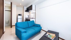 Un salon moderne avec un canapé bleu, une petite table sur laquelle repose un magazine, et une cuisine en arrière-plan.