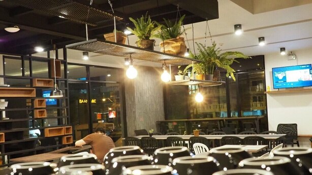 Un interior de restaurante con mesas, plantas colgantes e iluminación colgante.