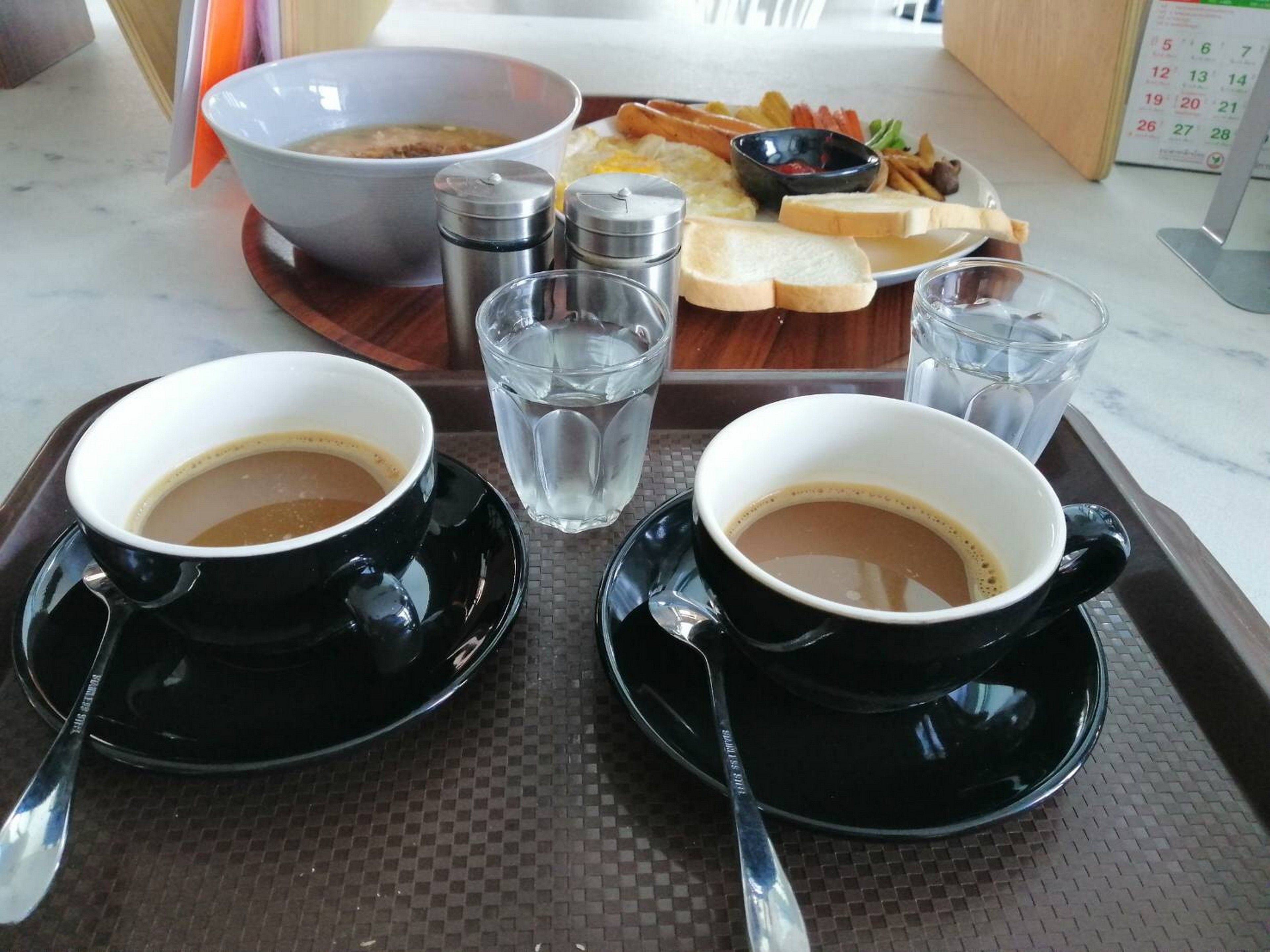 A tray with two black cups of coffee, a bowl of soup, and a plate of food including toast, eggs, and fries.