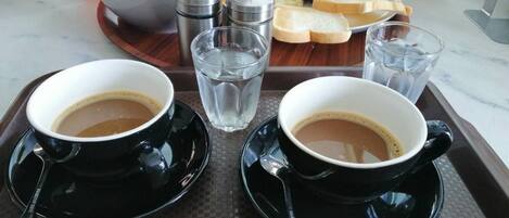 A tray with two black cups of coffee, a bowl of soup, and a plate of food including toast, eggs, and fries.