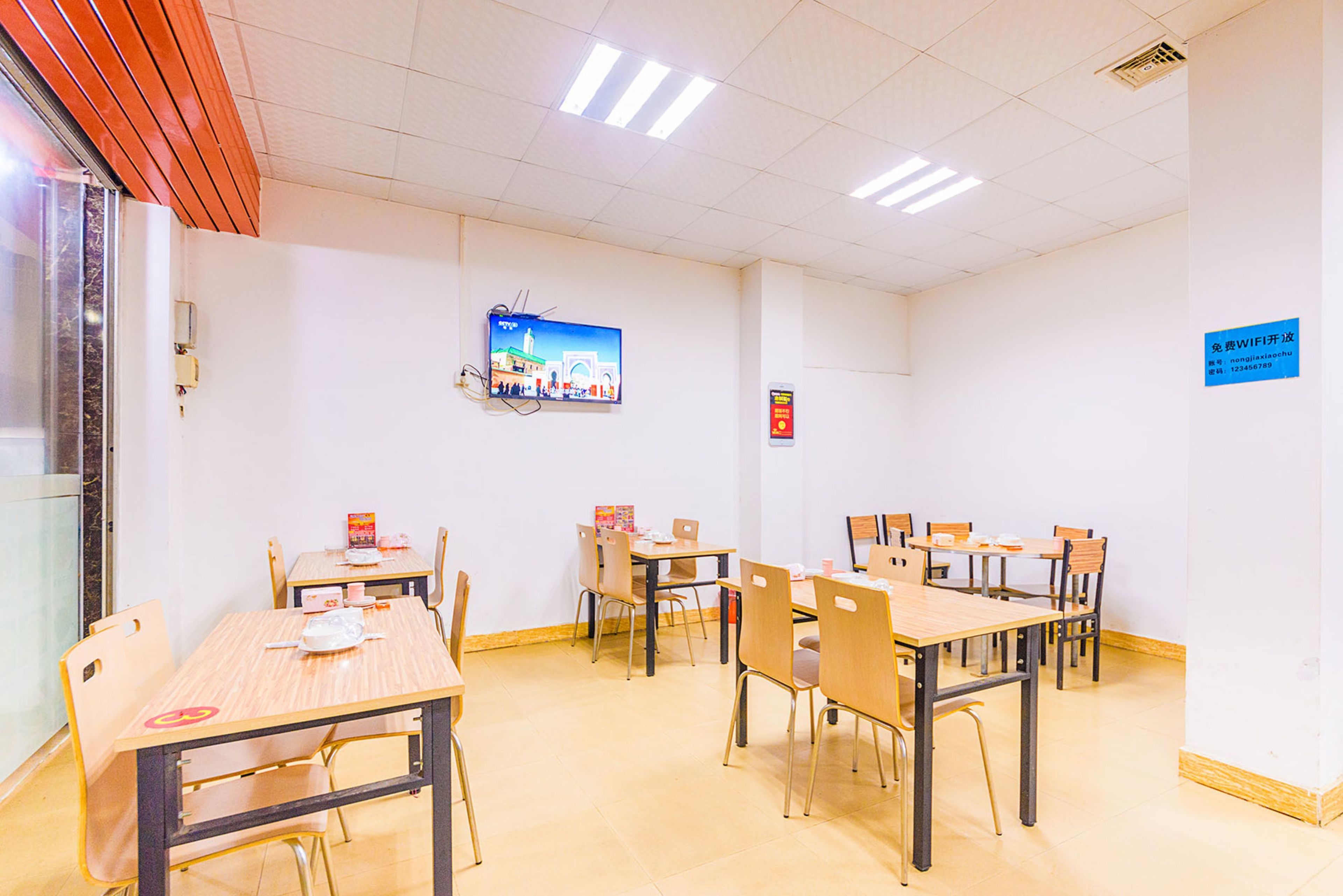 A conference room with multiple tables and chairs, a television mounted on the wall, and a sign indicating WiFi availability.