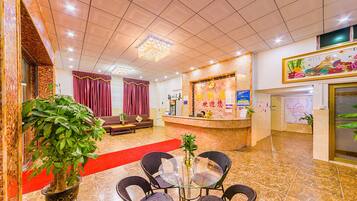 A hotel lobby with a reception desk, seating area, and a large potted plant.