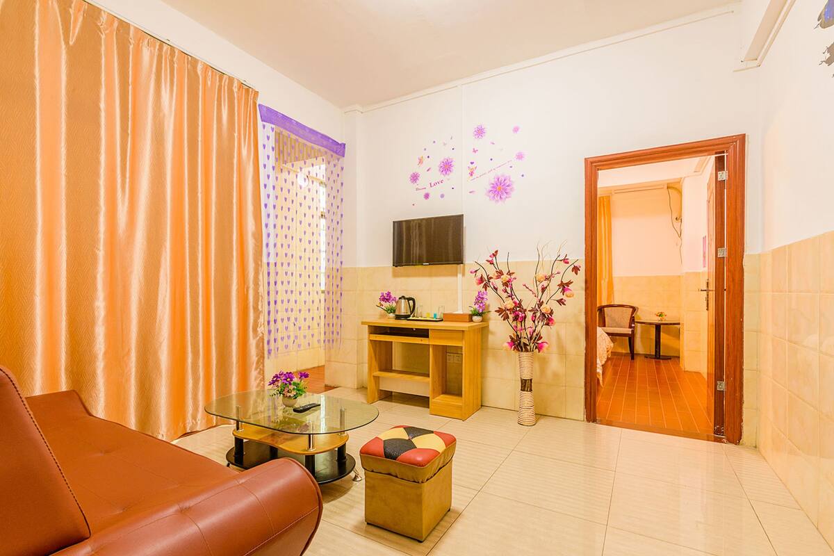 Uma sala de estar com um sofá de couro marrom, uma mesa de centro de vidro, uma mesinha de cabeceira de madeira, uma televisão e um vaso com flores.