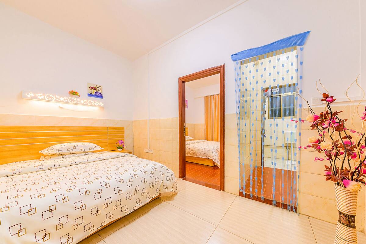 Quarto com cama, mesa de cabeceira, luminária na parede e porta que dá para outro espaço.