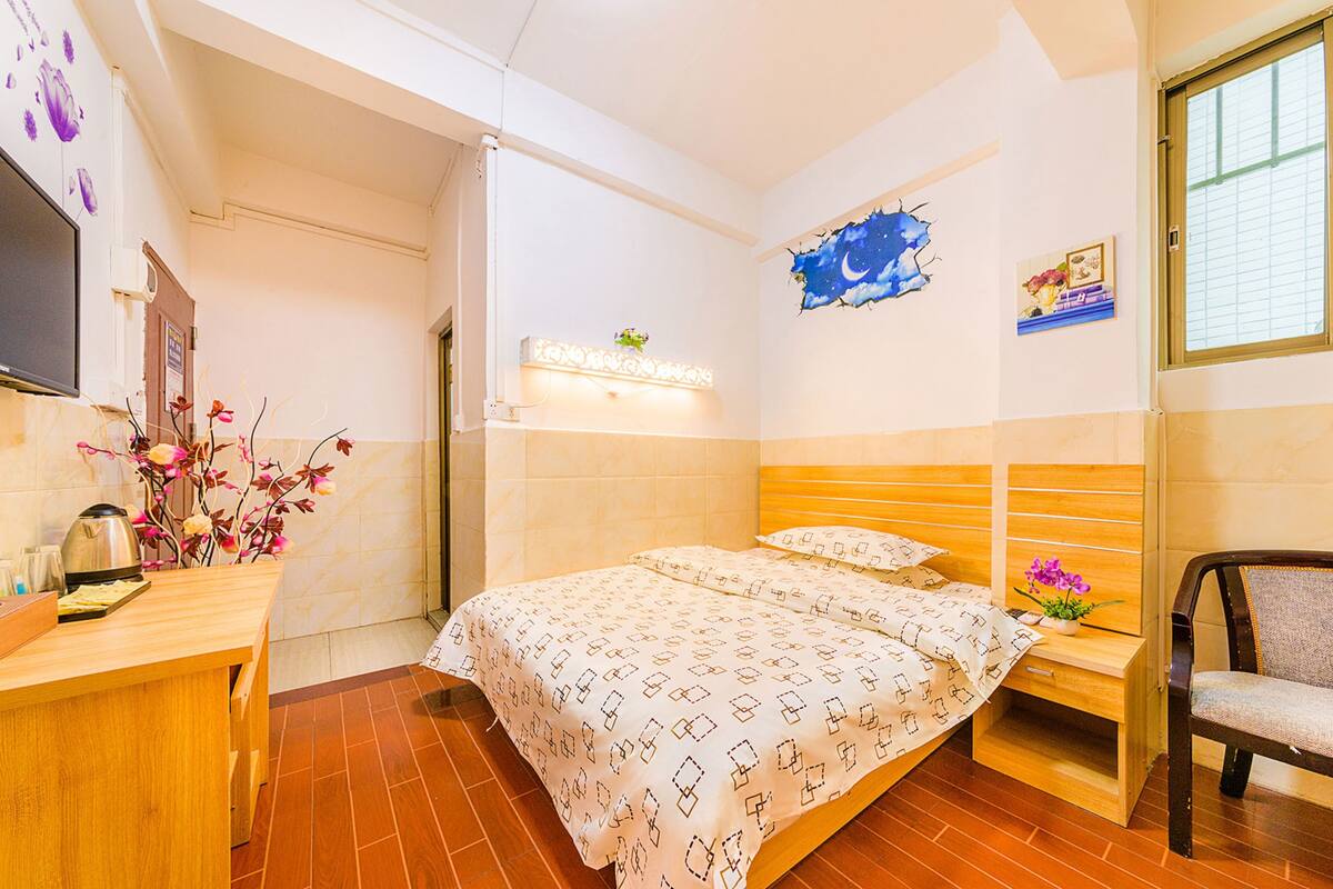 Quarto de hotel com cama, mesa de cabeceira, cadeira e televisão na parede.