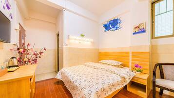 A hotel room with a bed, bedside table, chair, and a wall-mounted TV.
