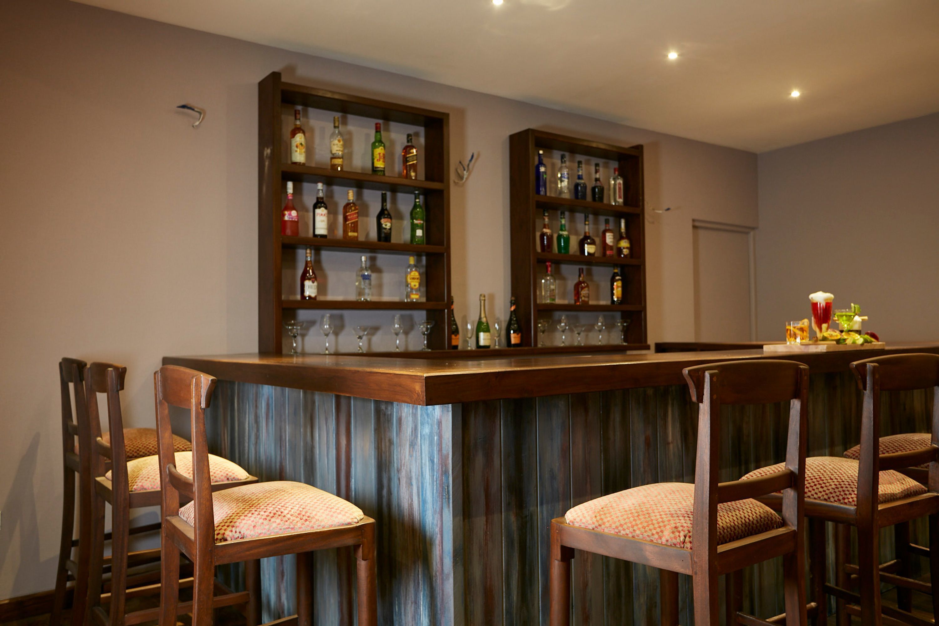 A bar area with wooden chairs, a counter with bottles, and shelves of liquor.