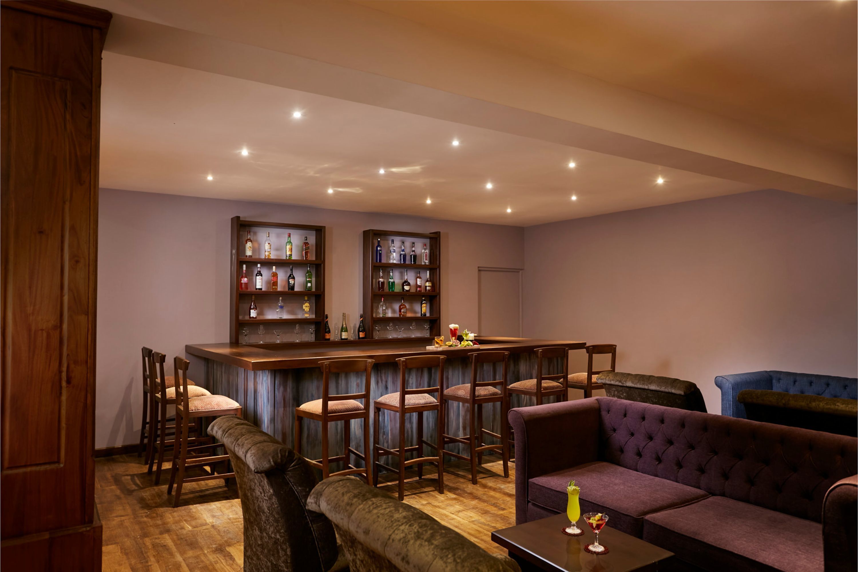 A bar area with wooden bar stools, a cushioned bench, and a purple sofa.