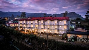 A multi-story hotel with a red roof, multiple balconies, and a well-lit entrance. - Galway Heights Hotel (Nuwara Eliya)