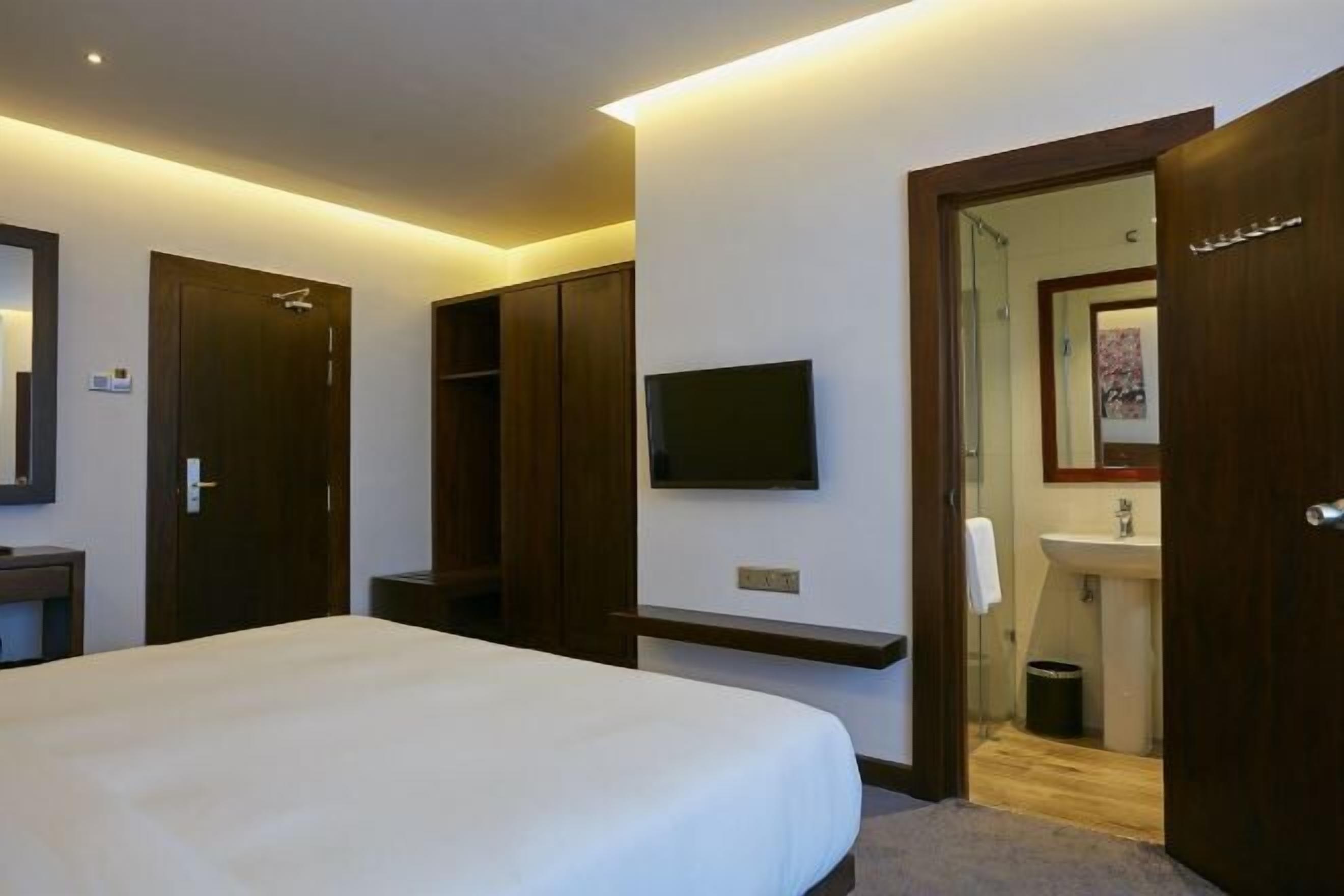 Une chambre d’hôtel comprenant un lit, une télévision, un miroir, une armoire et une salle de bain avec un lavabo et des toilettes.