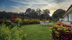 A well-maintained garden with a lawn, a seating area with white chairs, and a variety of colorful flowers. - Galway Heights Hotel (Nuwara Eliya)