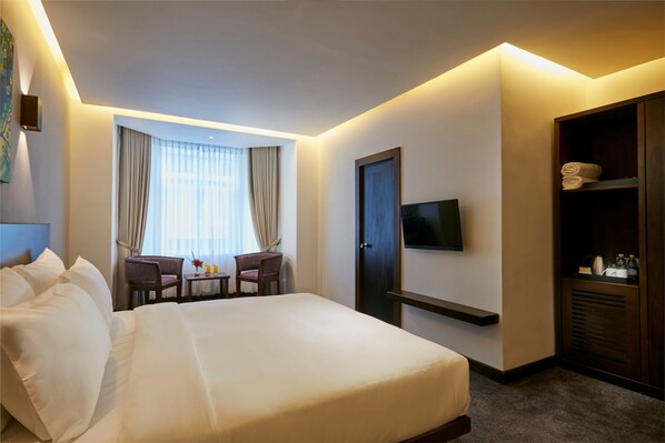 A hotel room with a large bed, a TV mounted on the wall, a desk with a chair, and a wardrobe.