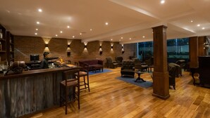 A spacious bar area with a wooden bar counter, multiple seating options including a red sofa and several armchairs, and a brick wall with built-in lighting. - Galway Heights Hotel (Nuwara Eliya)