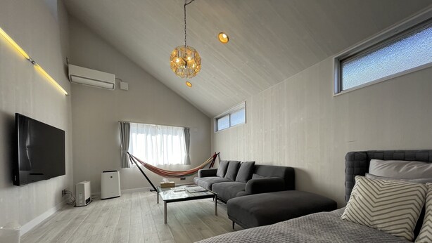 A modern living room with a large bed, a sofa, a coffee table, and a TV. There is a hammock, a window with curtains, and a ceiling light fixture. - tocoro. Mt. Fuji Hazuki (Fujikawaguchiko)