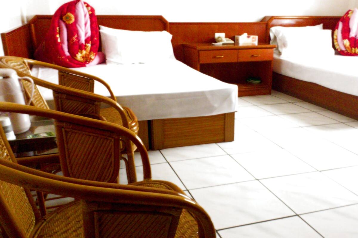 A hotel room with two beds, a wooden nightstand, a chair, and a small table.