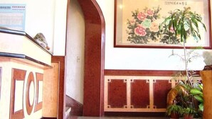 A reception area with a reception desk, a framed floral artwork, and potted plants. - Jin Lon Hotel (Taitung)