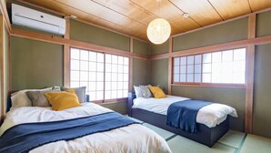 Ein traditioneller japanischer Raum mit Tatami-Matten, zwei Betten mit weißer und blauer Bettwäsche und einem Deckenventilator.