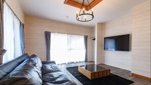 Ein modernes Wohnzimmer mit einer Ledersofa, einem Glastisch und einem flachbildfernseher an der Wand.