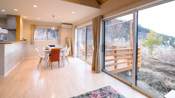 A spacious kitchen with a wooden countertop and modern appliances, a dining area with a table and chairs, and large windows offering a view of a wooden deck and surrounding landscape. - tocoro. Mt. Fuji Mutsuki (Fujikawaguchiko)
