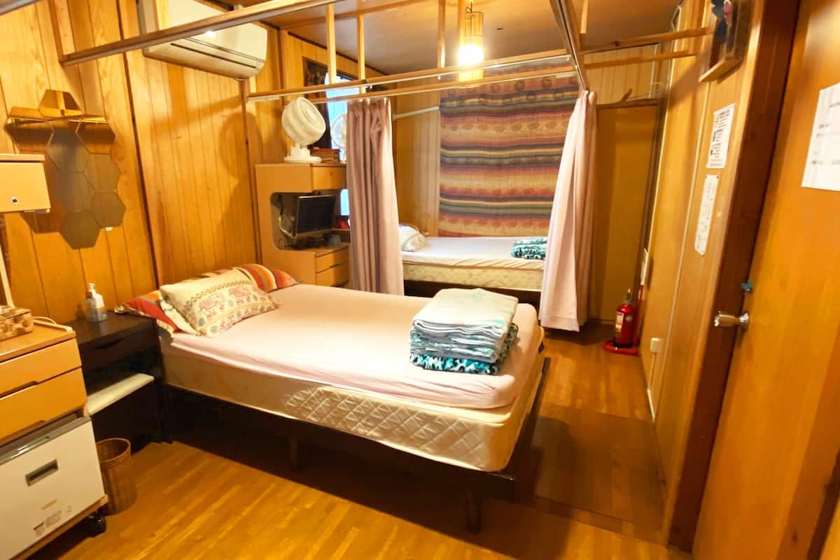 Habitación pequeña con cama, mesita de noche y ventilador.