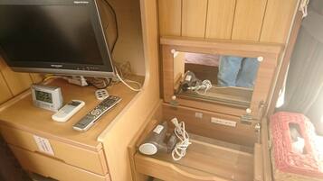 A wooden desk with a digital clock, a remote control, a hairdryer, and a mirror.