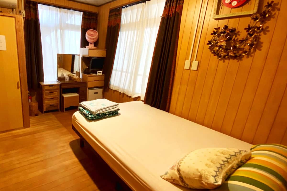Una habitación pequeña con una cama individual, un aparador, una tocador con espejo y un escritorio.