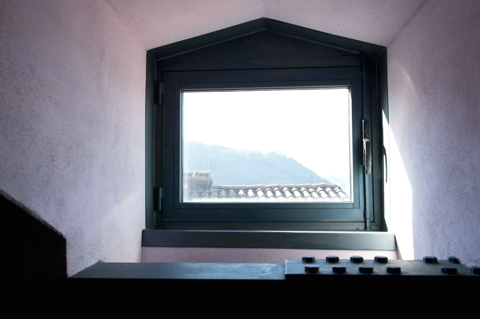 Une petite fenêtre à cadre noir donnant sur un bâtiment dont le toit est recouvert de tuiles.