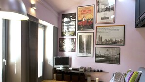 A living room with a TV, framed movie posters, a sofa, and a window with blinds.