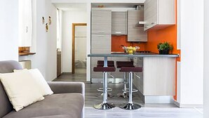 A modern kitchen with white cabinets, a central island with stools, and a dining area with a grey sofa. - Cernobbio Lake View (Cernobbio)