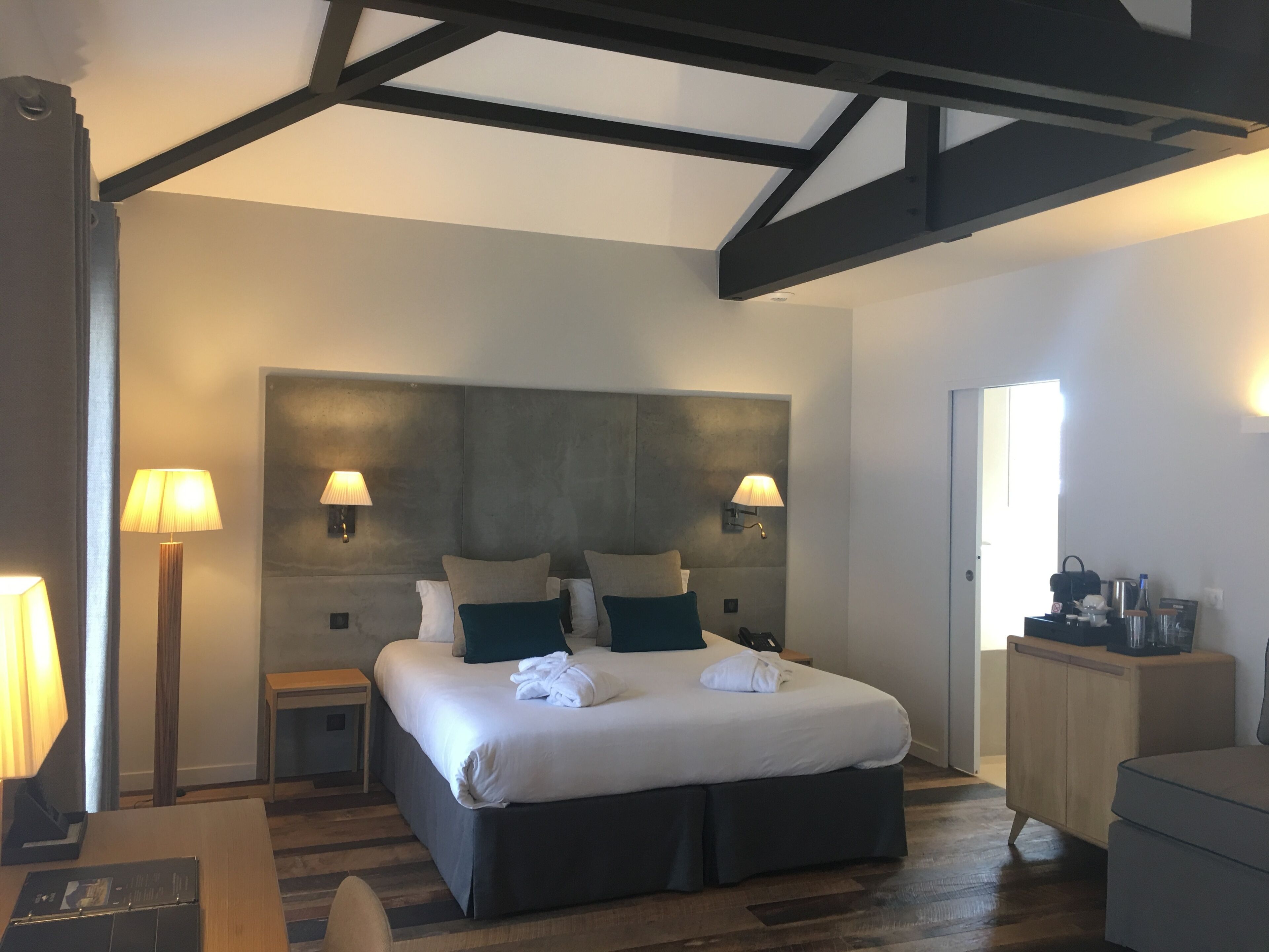 A hotel room with a large bed, two bedside lamps, a wooden headboard, a wooden nightstand, a wooden dresser, and a wooden chair.