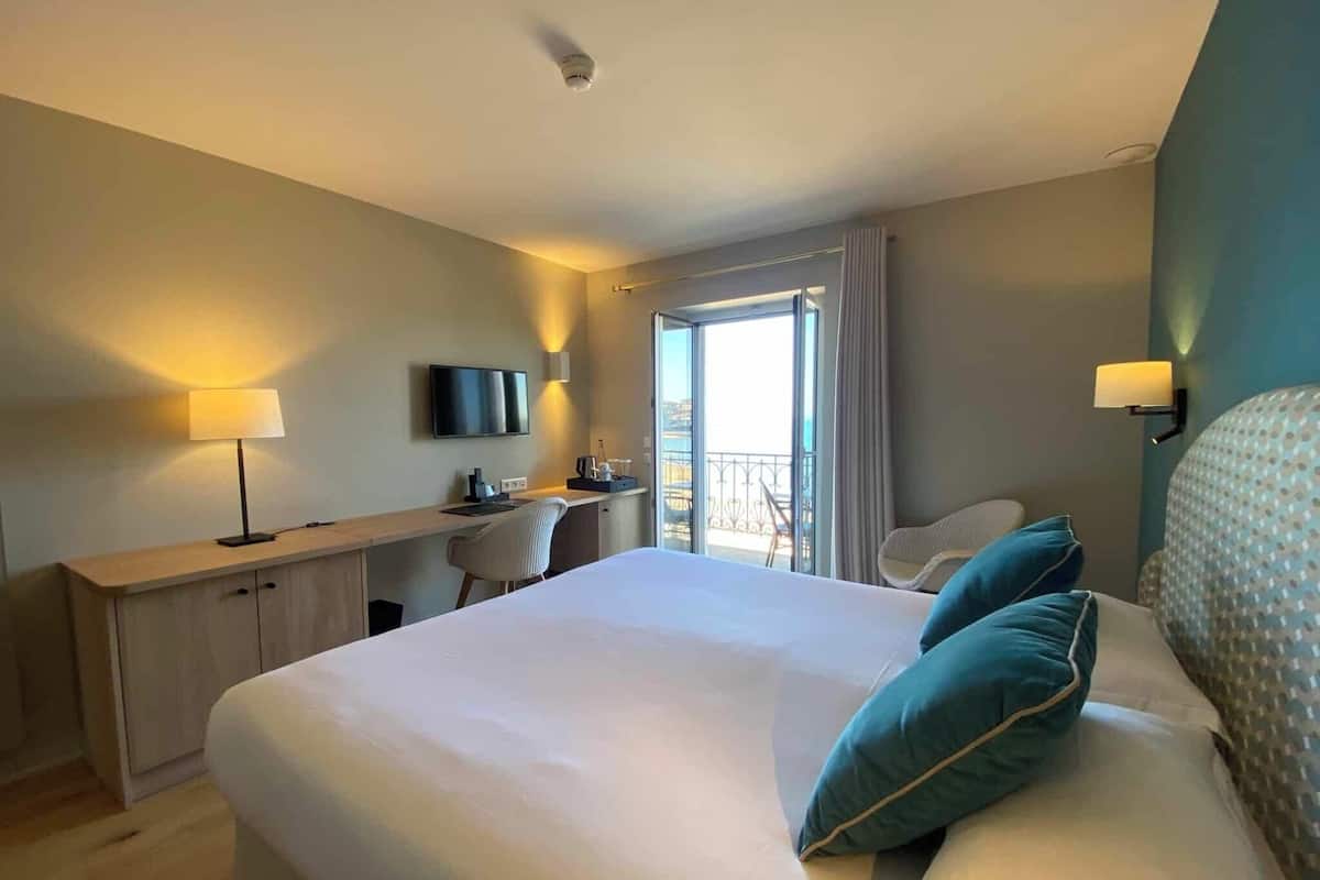 A hotel room with a large bed, a desk, a television, and a balcony with a view.