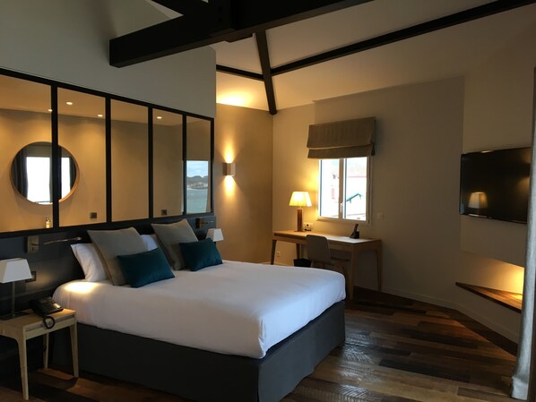 Habitación de hotel moderna con una cama grande, un escritorio, un televisor y un amplio ventanal con vistas.