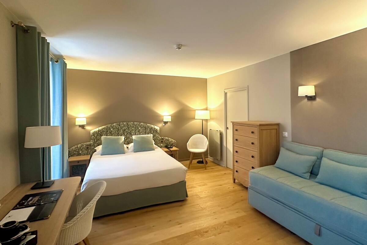 A hotel room with a bed, a desk, a chair, a dresser, and a sofa.