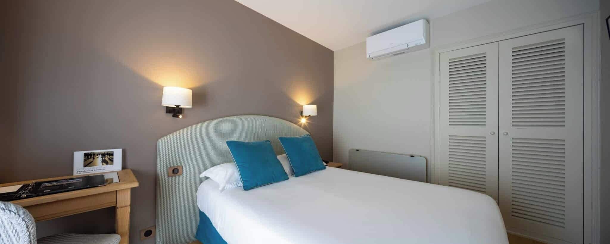 A hotel room with a bed, bedside lamps, a desk with a picture frame, and a wardrobe.
