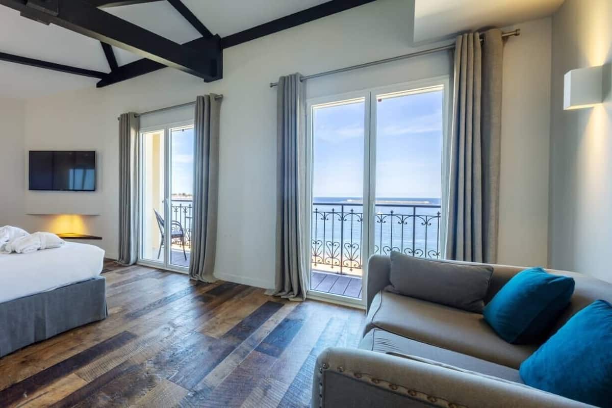 A hotel room with a bed, a sofa, a desk with a lamp, a TV, and a balcony with a view.