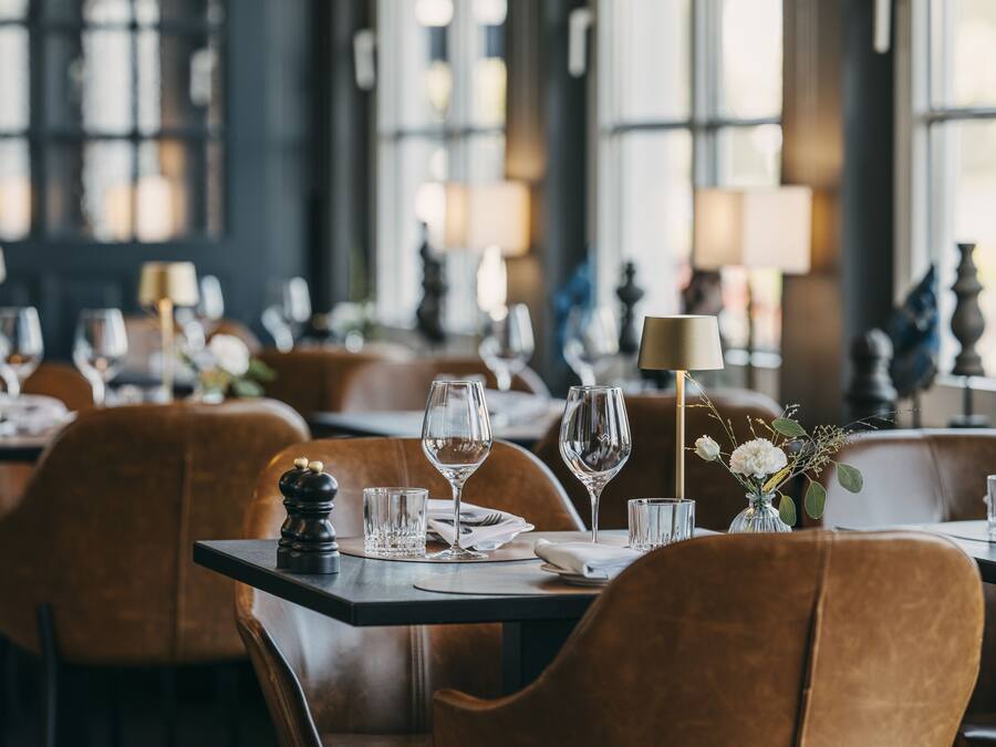A restaurant interior with tables set for dining, featuring brown leather chairs and clear glassware.