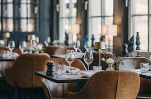 Interior de un restaurante con mesas dispuestas para comer, con sillas de cuero marrón y vasos de vidrio transparente.