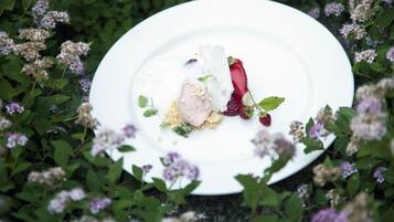 Un plato blanco con un postre sobre una mesa de jardín, rodeado de follaje y flores.