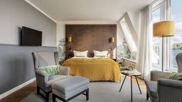 Una habitación de hotel moderna con una cama grande, dos sillones, una mesita y un televisor montado en la pared.