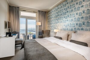 Habitación de hotel con cama, escritorio, silla y vista al agua con barcos.