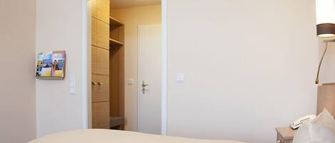 Una camera d'albergo con un letto, un comodino, una lampada e una porta che dà accesso a un armadio.