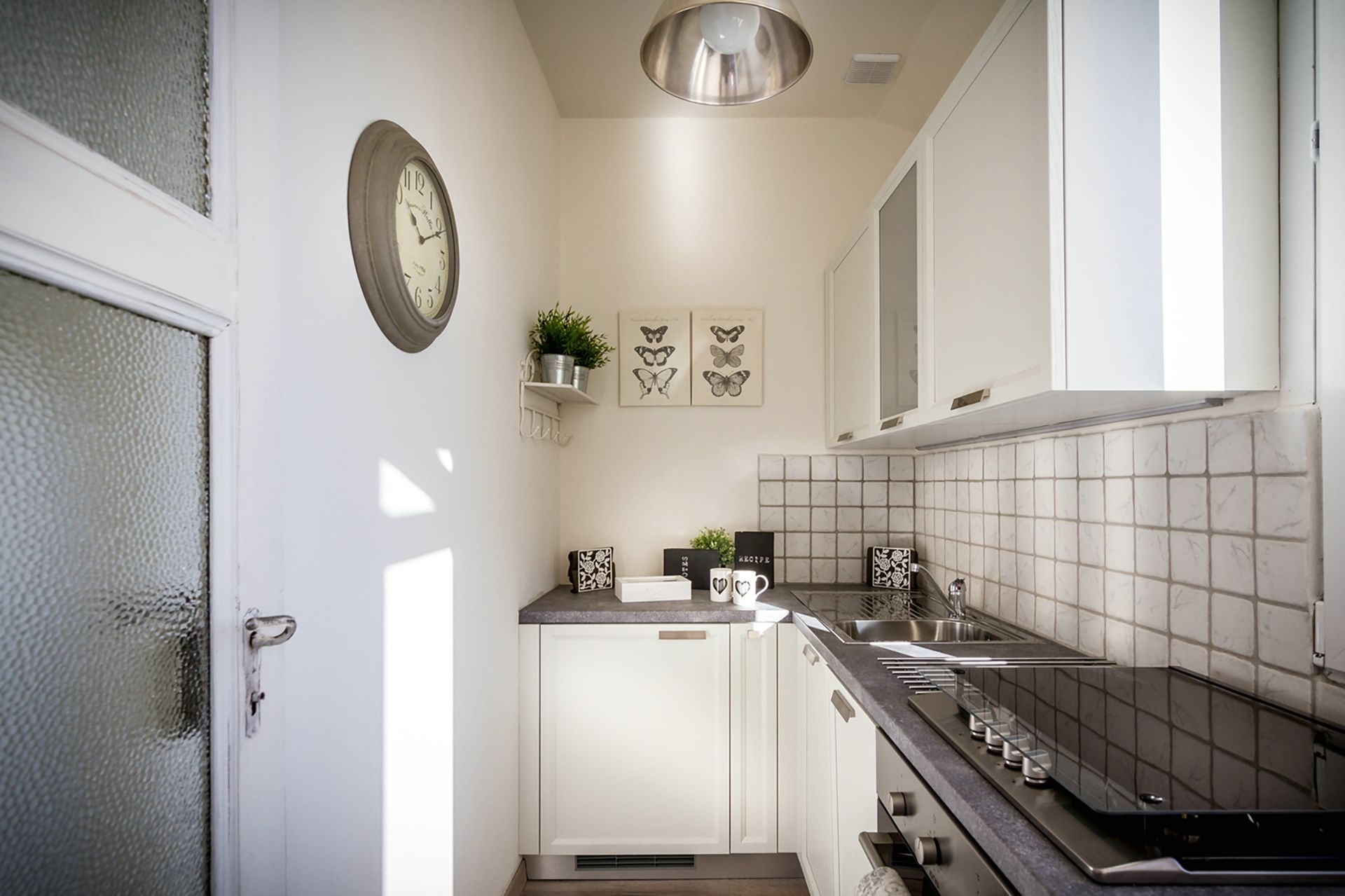 Una cocina moderna con armarios blancos, un lavamanos de acero inoxidable y una encimera negra. Hay un reloj en la pared y una planta en la encimera.