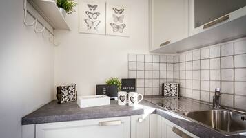 Een keuken met witte kastjes, een granieten aanrecht, een roestvrijstalen spoelbak en decoratieve elementen, waaronder een plant, een lijst met vlinderkunst en een receptbord.
