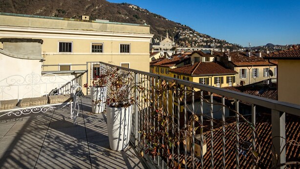 A balcony with a view of a hillside town, featuring terracotta-roofed buildings and a clear blue sky.