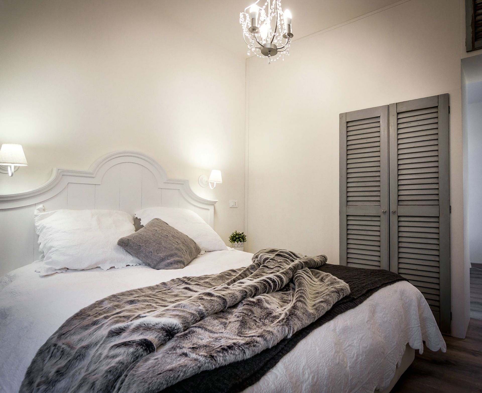 Un dormitorio con cama, candelabro, mesita de noche con lámpara y armario.